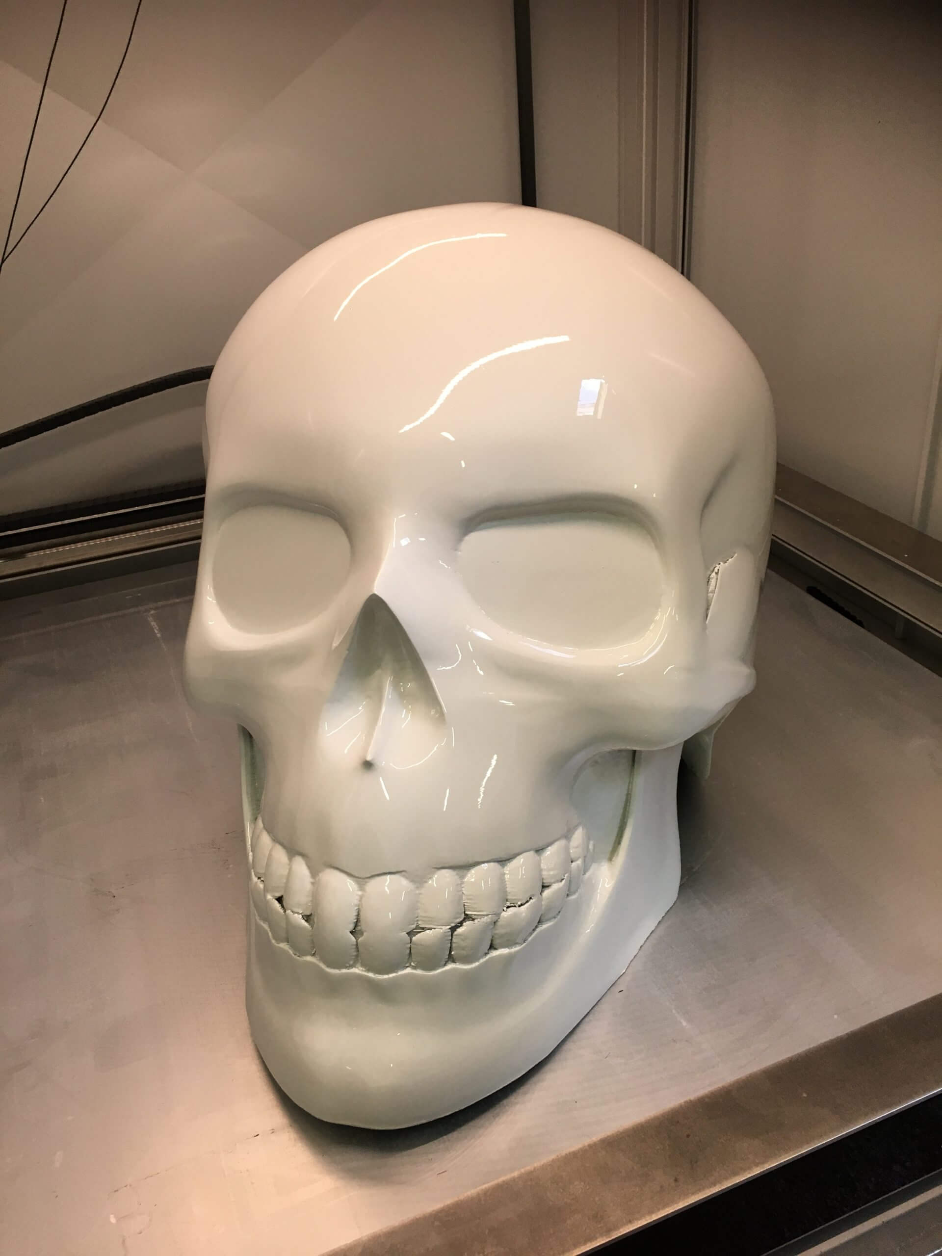 Crâne décoratif 3D blanc en plastique brillant, présenté sur une surface métallique, objet design et artistique
