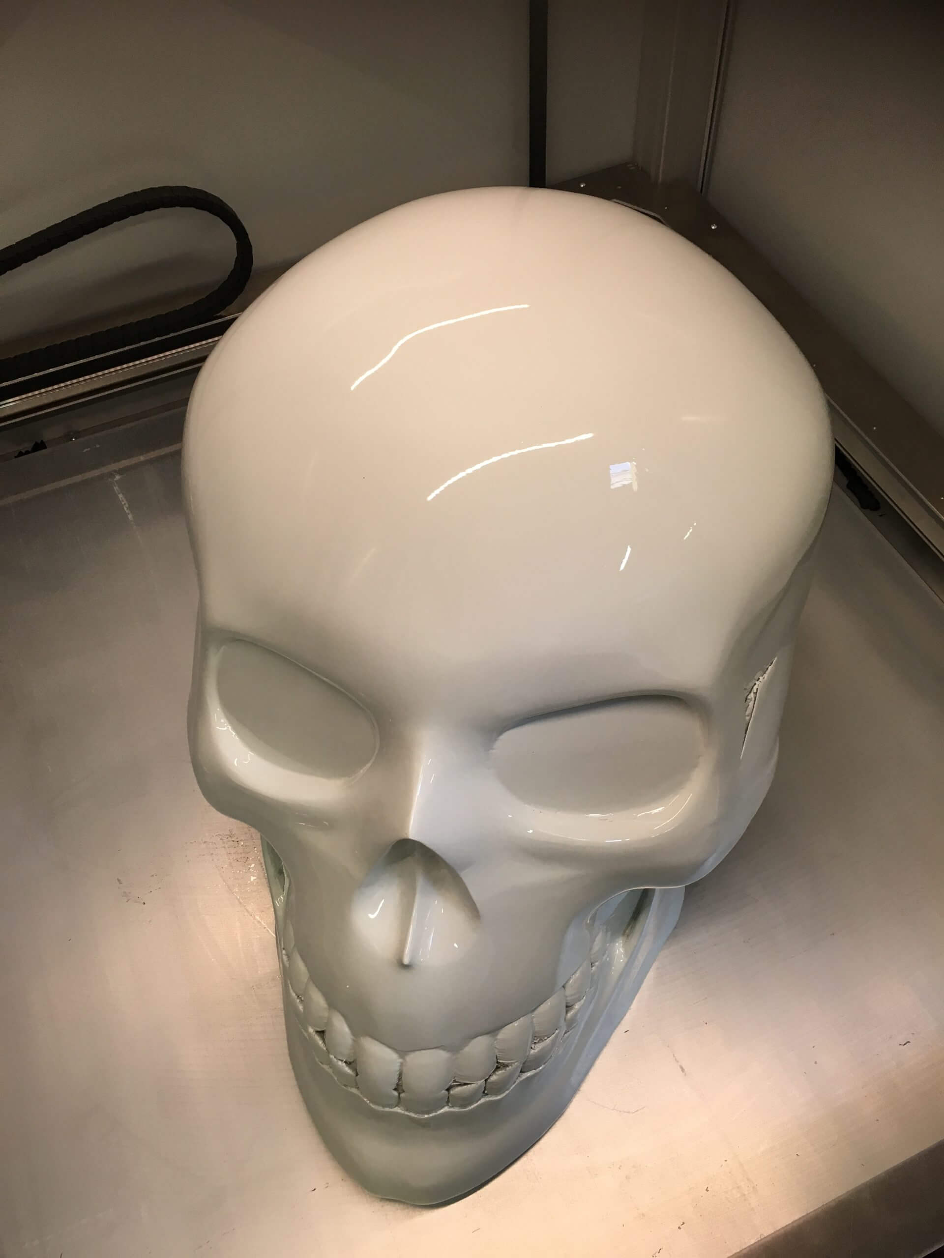 Crâne décoratif 3D blanc en plastique brillant, présenté sur une surface métallique, objet design et artistique