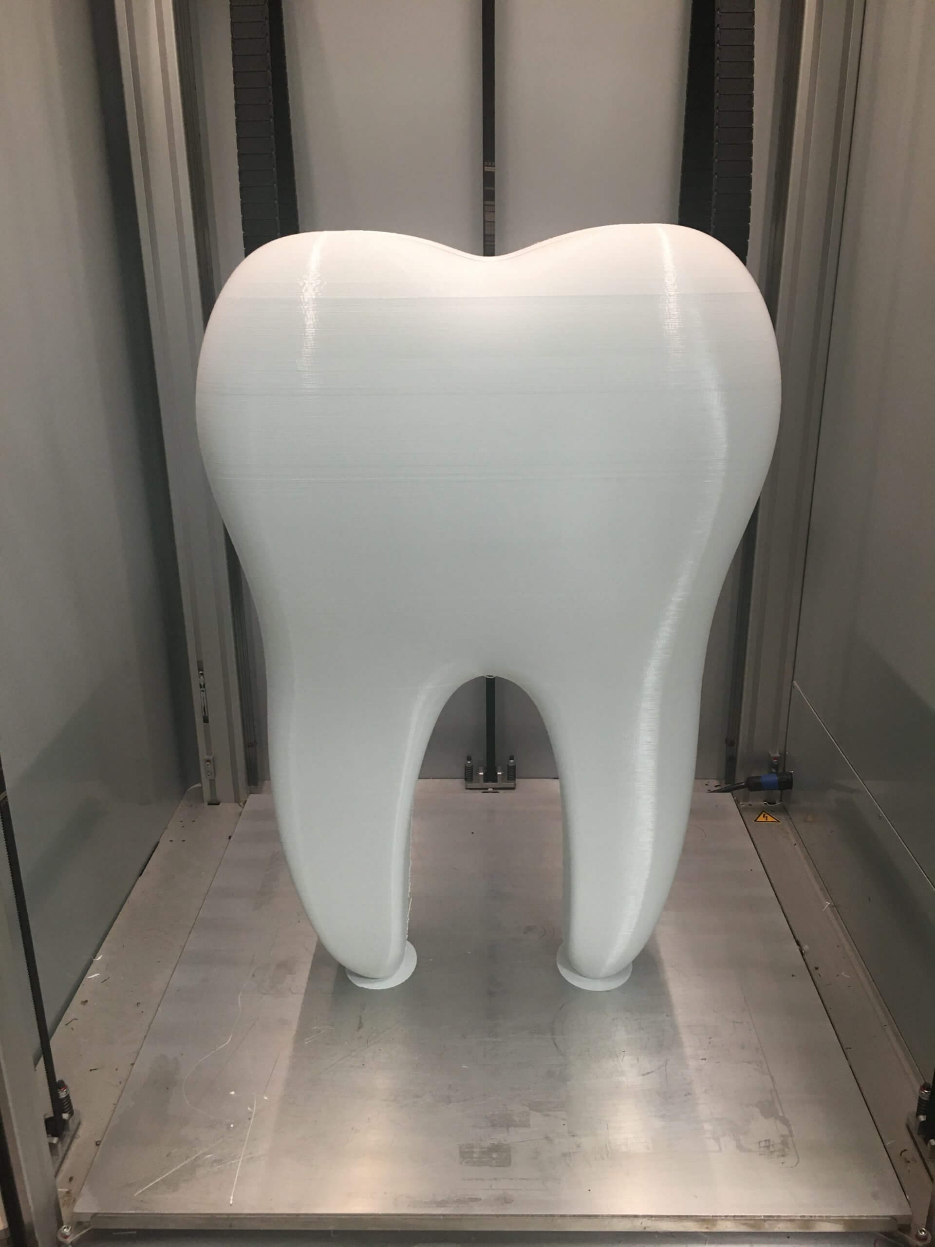 Dent blanche imprimée en 3D grand format, présentée dans une machine d'impression 3D, utilisée en médecine dentaire