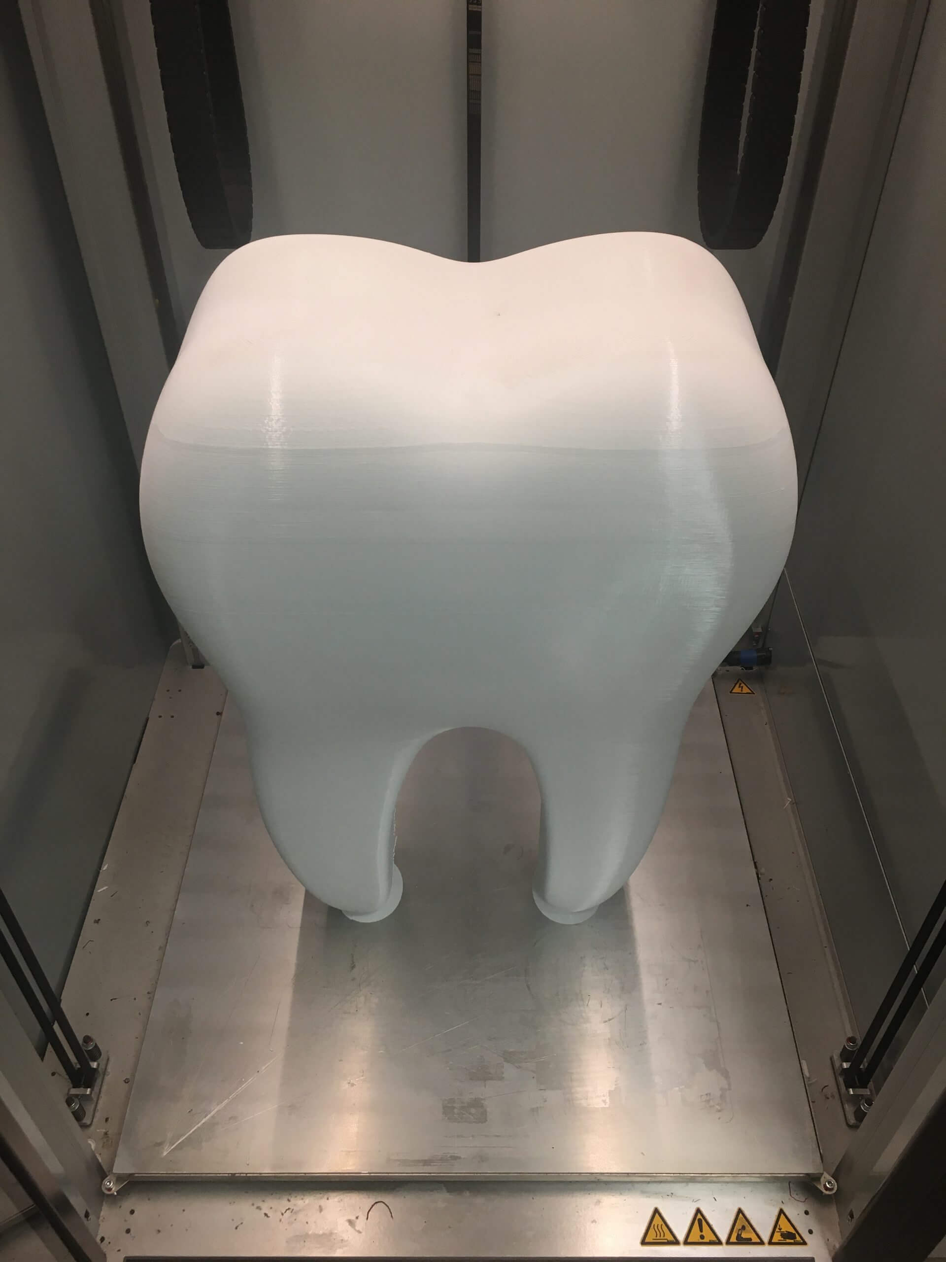 Modèle de dent blanche imprimée en 3D grand format, utilisé en médecine dentaire, présenté dans une machine d'impression 3D