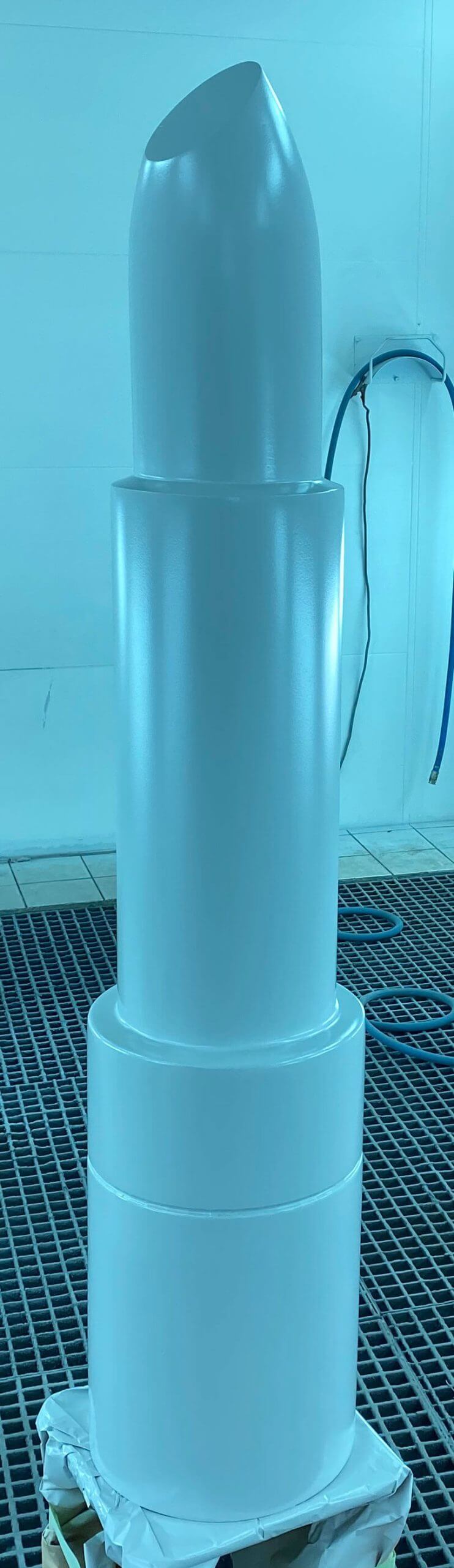 Objet blanc cylindrique imprimé en 3D grand format, ressemblant à un rouge à lèvres apprêté, présenté dans un atelier d'impression 3D.