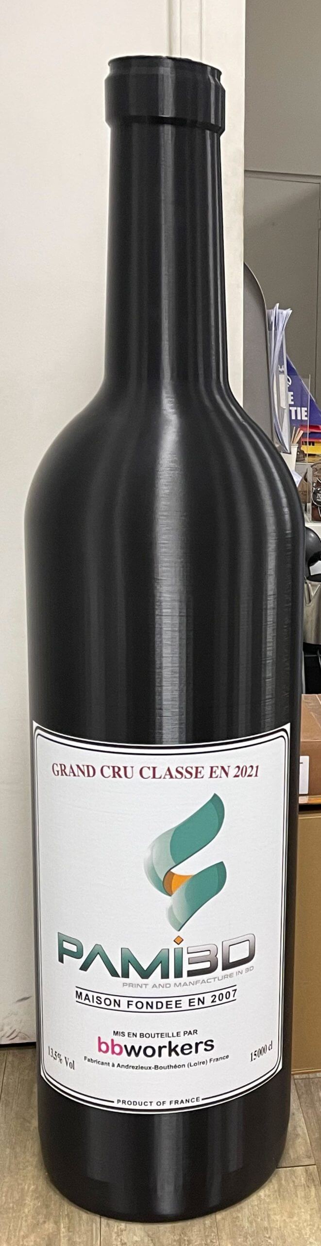 Bouteille noire haute avec étiquette PAMI3D imprimée en 3D grand format, posée sur une surface en bois.