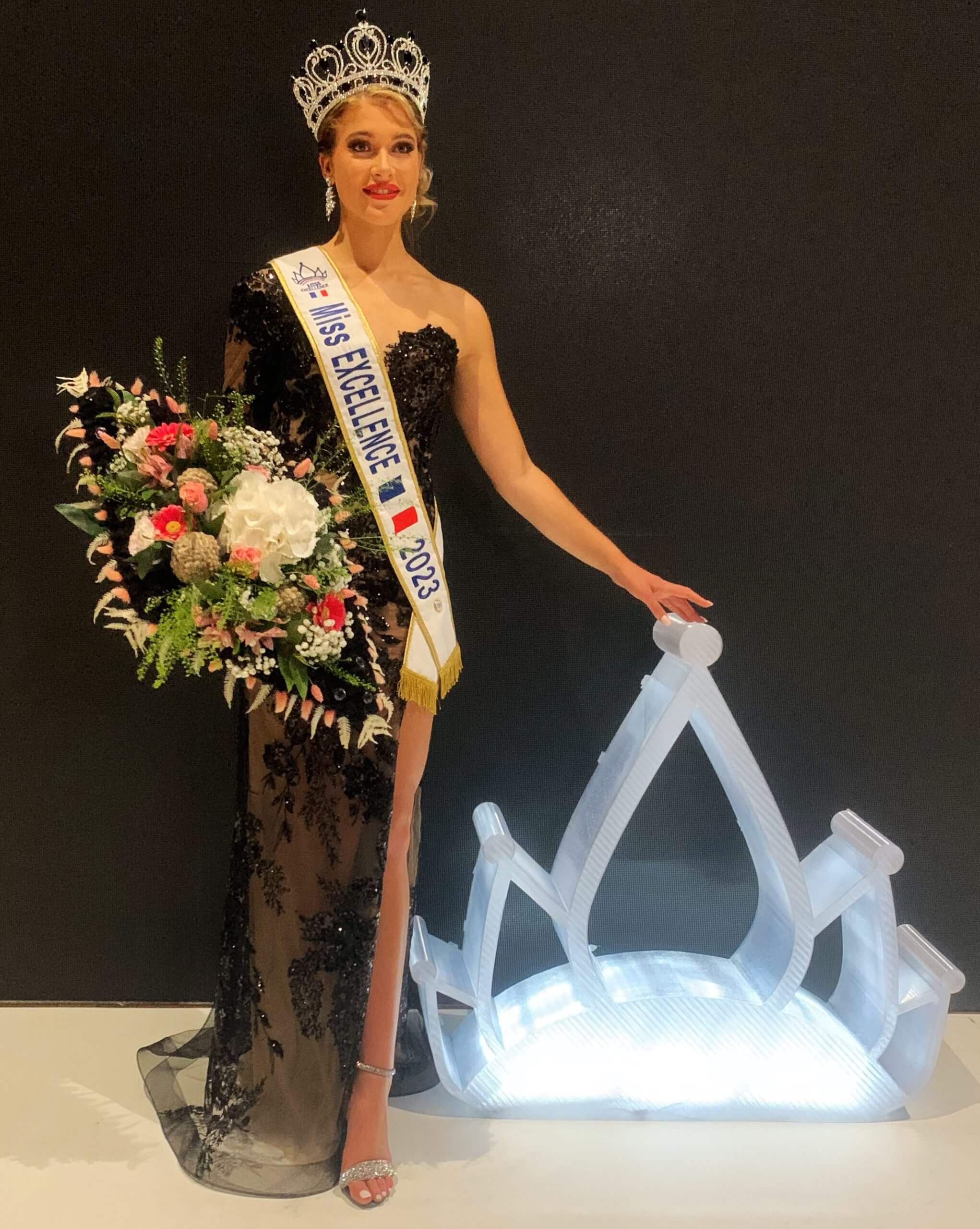 Miss Excellence posant avec une couronne 3D grand format illuminée, vêtue d'une robe noire élégante et tenant un bouquet de fleurs