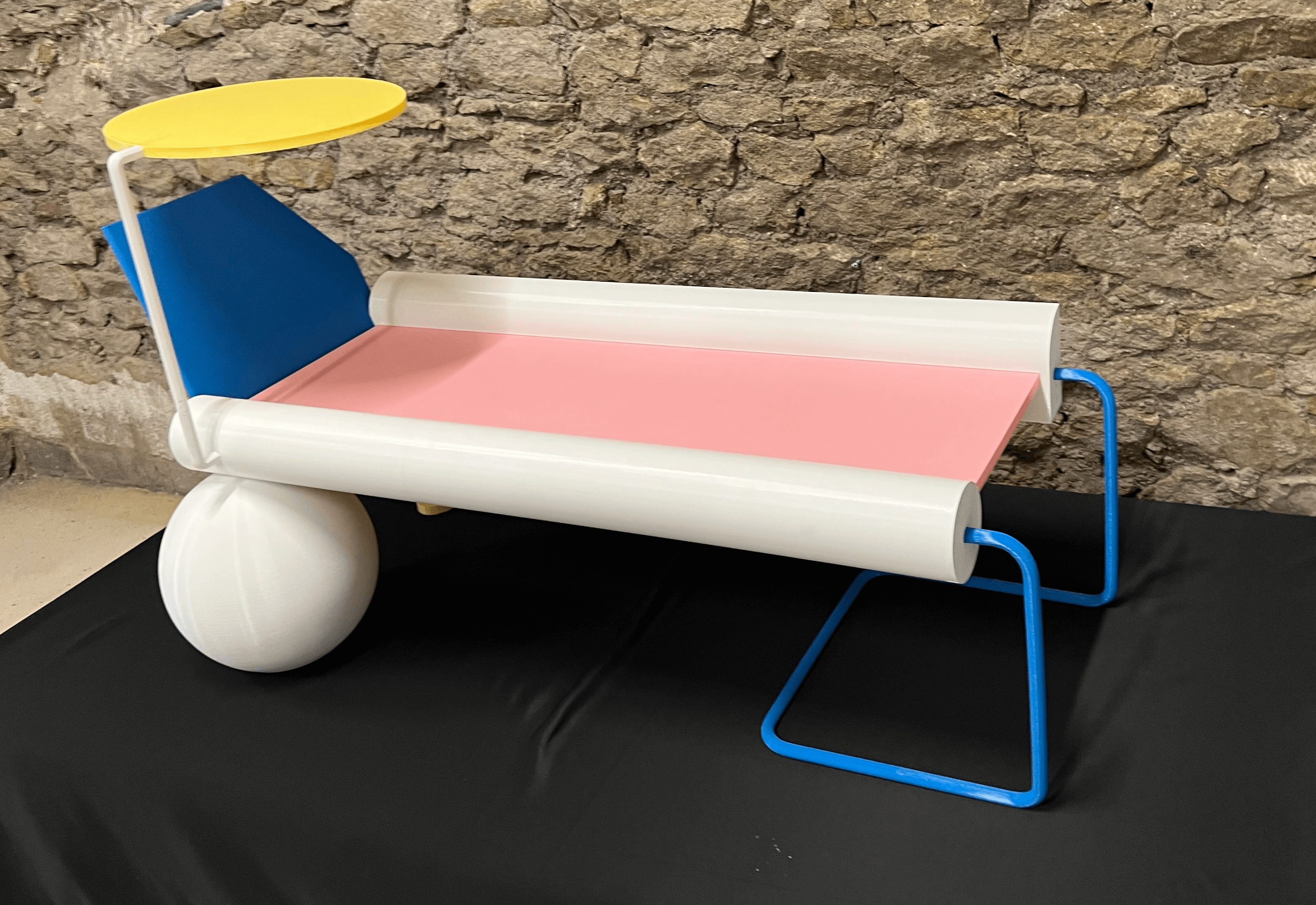 Transat design coloré en impression 3D grand format, avec structure blanche, assise rose, dossier bleu et parasol jaune, présenté sur fond pierre